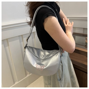 Detail of silver textured crossbody bag featuring pink butterfly embroidery and flap closure