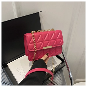 Detail of rose red quilted crossbody bag with gold chain strap and metal clasp on box