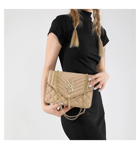 Detail der beigen Stepptasche mit goldenem Logo, Kette und elegantem Quastenanhänger
