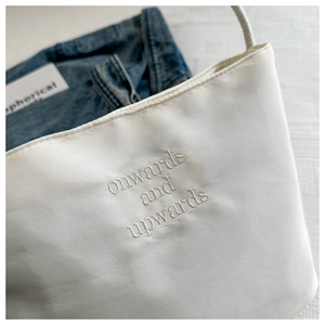 Dettaglio della borsa tote in tela bianca con ricamo onwards and upwards su denim
