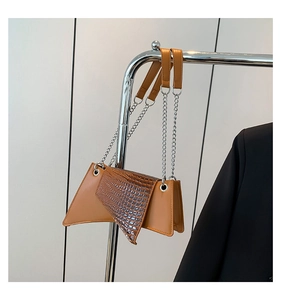 Detail of asymmetrical brown crossbody bag with faux crocodile texture and silver chain
