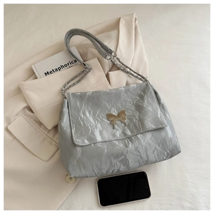 Detail of silver flap bag with gold butterfly clasp and chain strap on aesthetic background