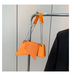 Detail of bright orange patent leather trapezoid handbag with crocodile texture and silver chain