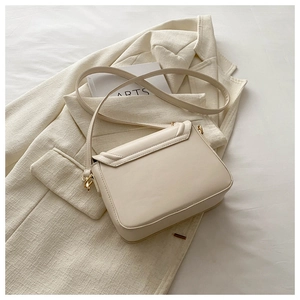 Détail d'un petit sac à bandoulière crème avec boucle dorée posé sur une veste