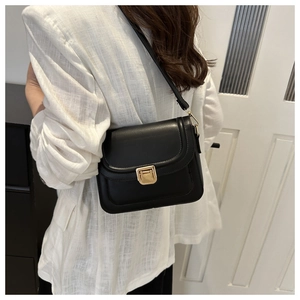 Sac bandoulière en cuir lisse noir avec fermoir doré porté sur un costume blanc élégant