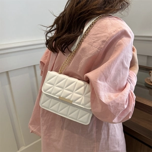 White quilted crossbody bag with gold chain strap shown on a model in a casual setting