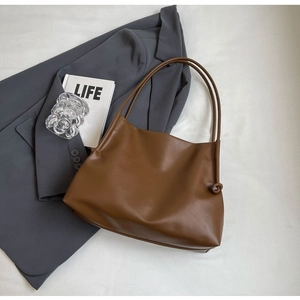 Dettaglio di una borsa tote in pelle marrone scuro con decoro a nodo su stoffa