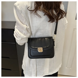 Détail d'un sac bandoulière noir avec boucle dorée porté par un mannequin en blazer
