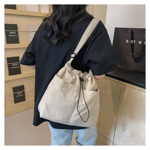 Detail of beige drawstring crossbody bag with front pocket and adjustable black strap