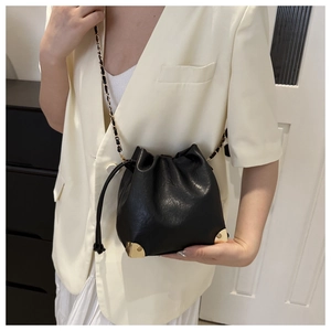 Detail of black drawstring bucket bag featuring gold metal corners and chain strap