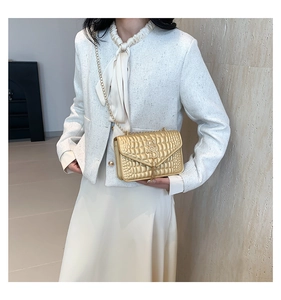 Détail d'un sac bandoulière doré motif crocodile avec pompon en métal et chaîne