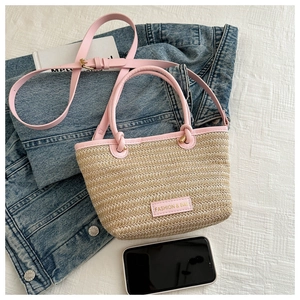 Close-up of beige woven bucket bag with pink leather handles and fashion logo label