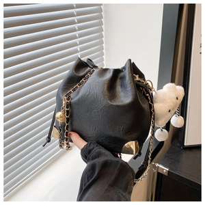 Detail of black drawstring bucket bag with gold chain strap and metal corner accents