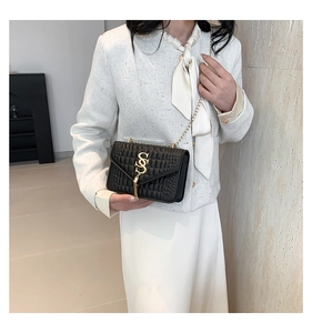 Détail du sac bandoulière matelassé noir avec logo SS doré et pompon sur veste en tweed