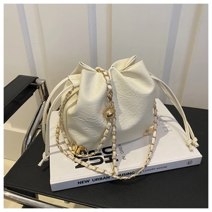 Detail view of a white drawstring bucket bag featuring gold chains on a book surface