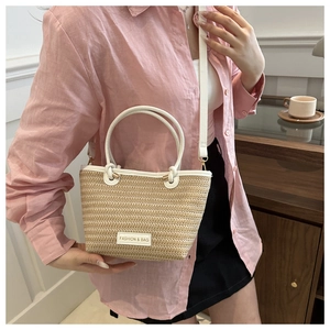 Detail view of woven straw bucket bag with white leather handle and fashion tag