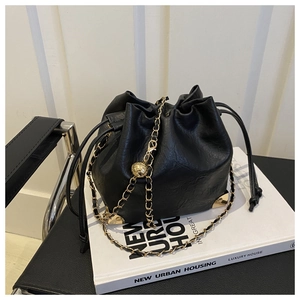 Detail of black drawstring bucket bag featuring gold metal corners and chain strap with charm