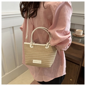 Detail of hand-woven beige straw bucket bag with white leather straps and fashion label