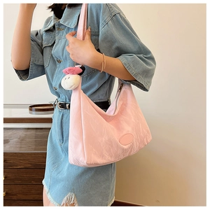 Detail of pink pleated shoulder bag with white fluffy charm and oval logo on the model