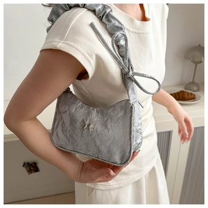 Detail of silver metallic pleated shoulder bag featuring a butterfly buckle and scrunchie strap