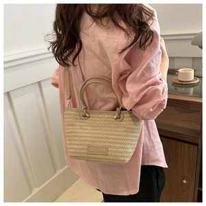 Detail of woven straw bucket bag showing leather handles and fine texture in a home setting
