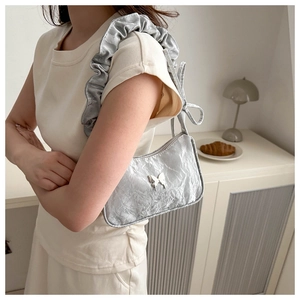 Detail of silver pleated shoulder bag featuring metal butterfly and ruffled strap design