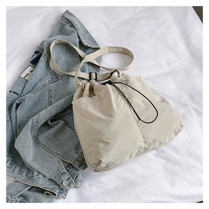 Detail of beige drawstring crossbody bag with adjustable strap on white fabric background