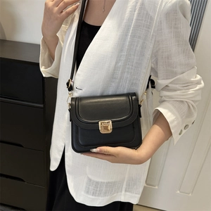 Sac bandoulière classique en cuir noir avec fermoir doré porté sur une veste blanche