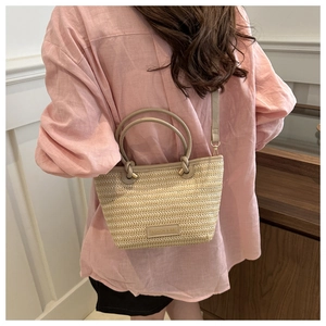 Straw bucket bag with round handles and shoulder strap shown on model in a cozy interior