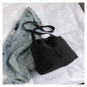Detail of black drawstring nylon tote bag with texture and strap on white fabric