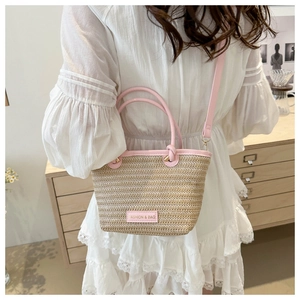 Detail of hand-woven straw bucket bag with pink leather trim and logo tag shown in a room