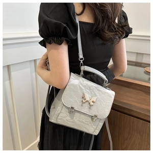 Close-up of a grey shiny pleated mini backpack with a silver butterfly metal ornament