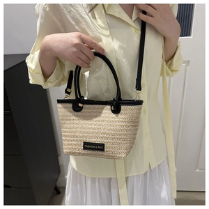 Detail of woven straw bucket bag with black leather trim and gold metal hardware
