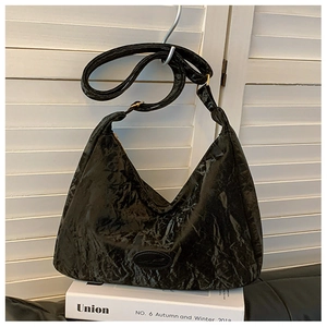 Detail of black pleated crescent shoulder bag featuring a glossy texture and branded patch