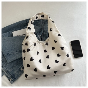Gros plan d'un sac cabas en satin blanc avec imprimés cœurs noirs et accessoires
