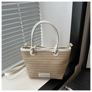 Detail of woven straw bucket bag with white leather handles and fashion logo patch