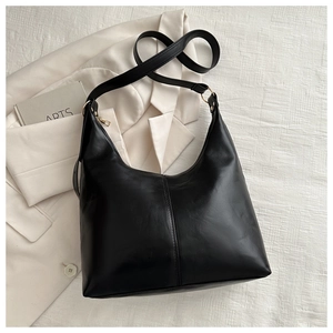 Top view of a minimalist black leather tote bag on beige textured fabric for office commute
