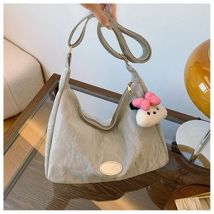 Close-up of light gray wrinkled hobo bag with pink bow plush charm and metallic logo
