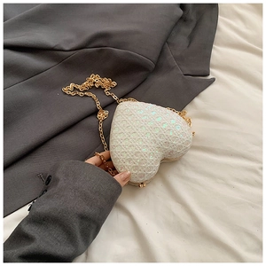 Close-up of white sequined heart-shaped bag with gold chain on grey blazer
