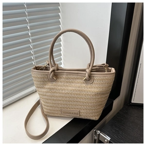 Close-up of beige woven straw bucket bag with brown leather handles and brand tag
