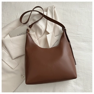 Detail view of brown leather tote bag with adjustable strap on beige blazer background
