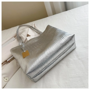Detail of silver crocodile pattern tote bag with metallic sheen and golden logo tag