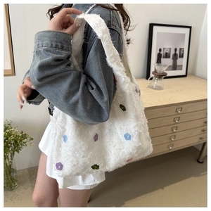 Détail de broderies florales colorées sur un sac cabas blanc à texture peluche
