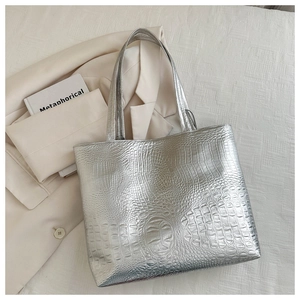Flat lay of a silver crocodile pattern tote bag with shoulder straps on a white linen bed