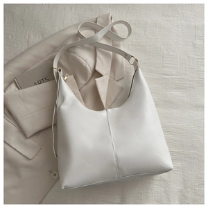 Detail of white leather hobo shoulder bag with central stitching on beige blazer