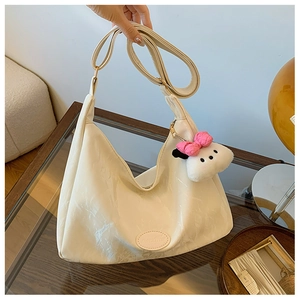 Detail of cream white crescent tote bag with plush charm and adjustable strap