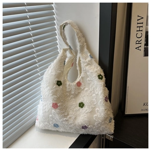 Détail de motifs floraux brodés colorés sur un sac cabas blanc à texture frangée