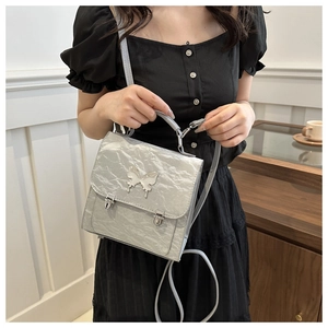 Detail of silver textured PU leather handbag with butterfly clasp worn by a model