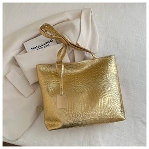 Detail of gold crocodile embossed tote bag texture with metallic tag and shoulder strap