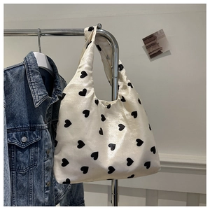 Gros plan du sac cabas en satin crème avec imprimés cœurs noirs sur un cintre en métal